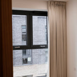 Beige curtain hanging in front of a window with a view of a building exterior.