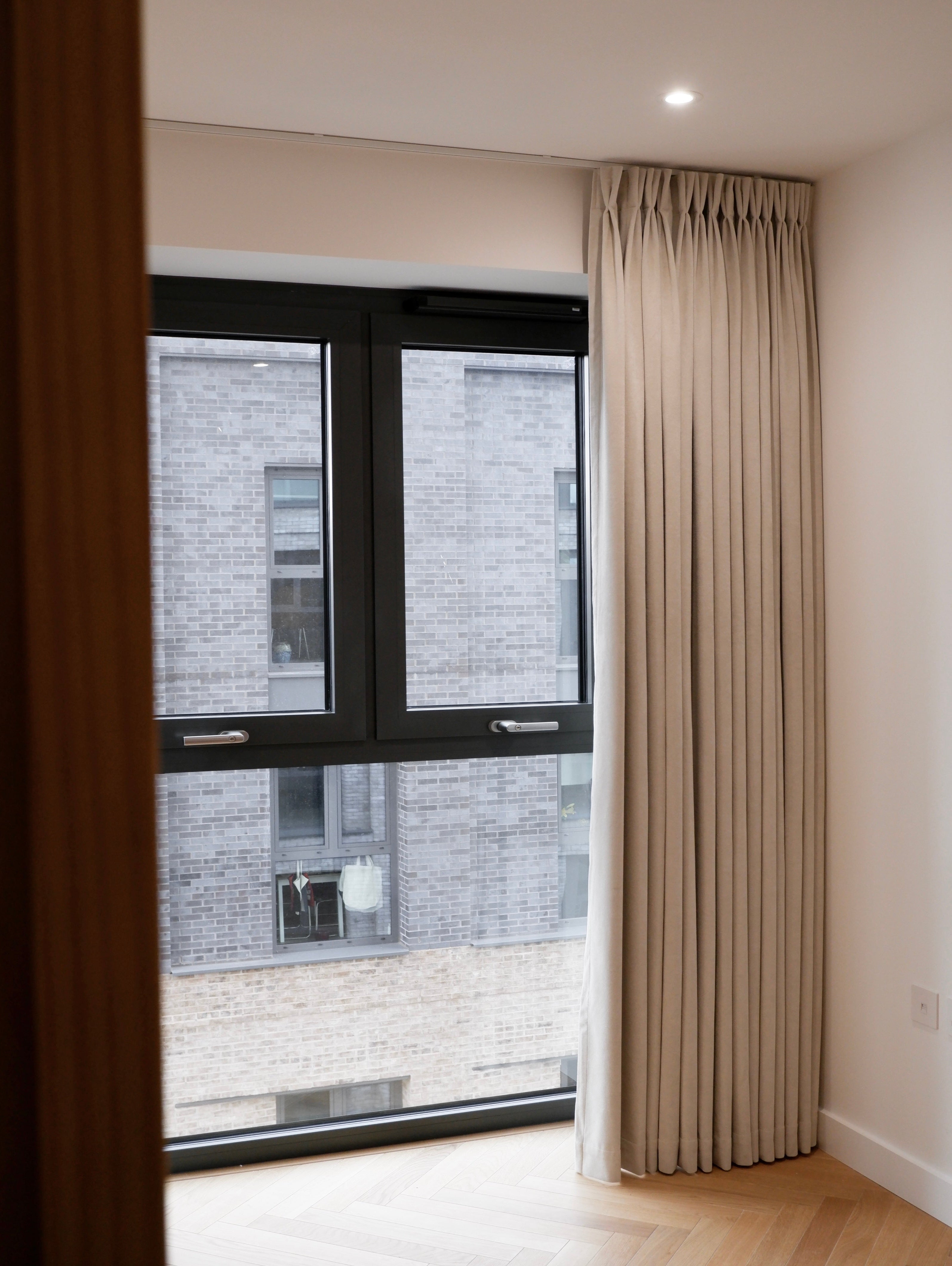 Beige curtain hanging in front of a window with a view of a building exterior.