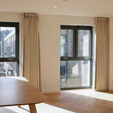 Modern room with large windows, beige curtains, and a wooden table.