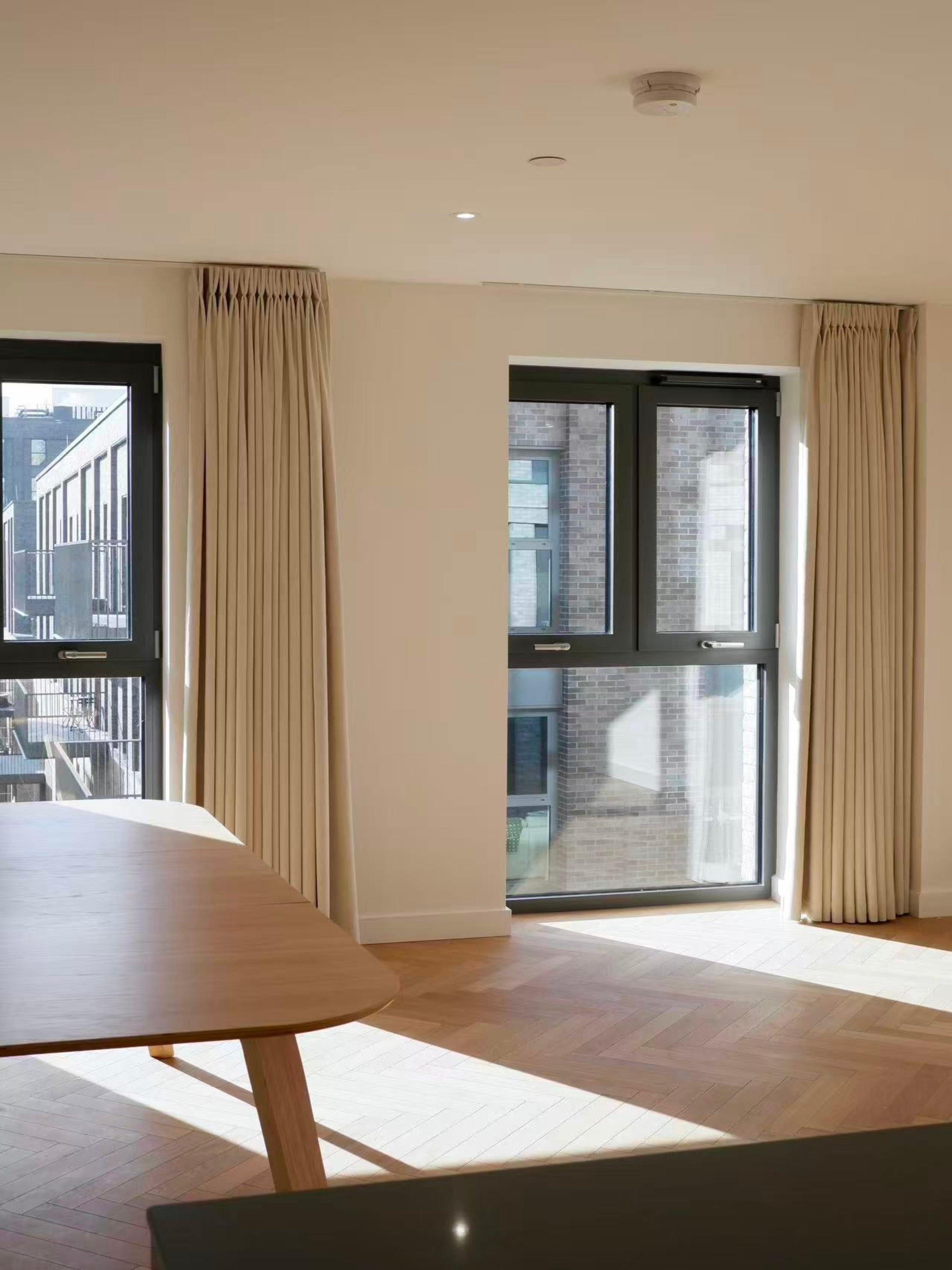 Modern room with large windows, beige curtains, and a wooden table.